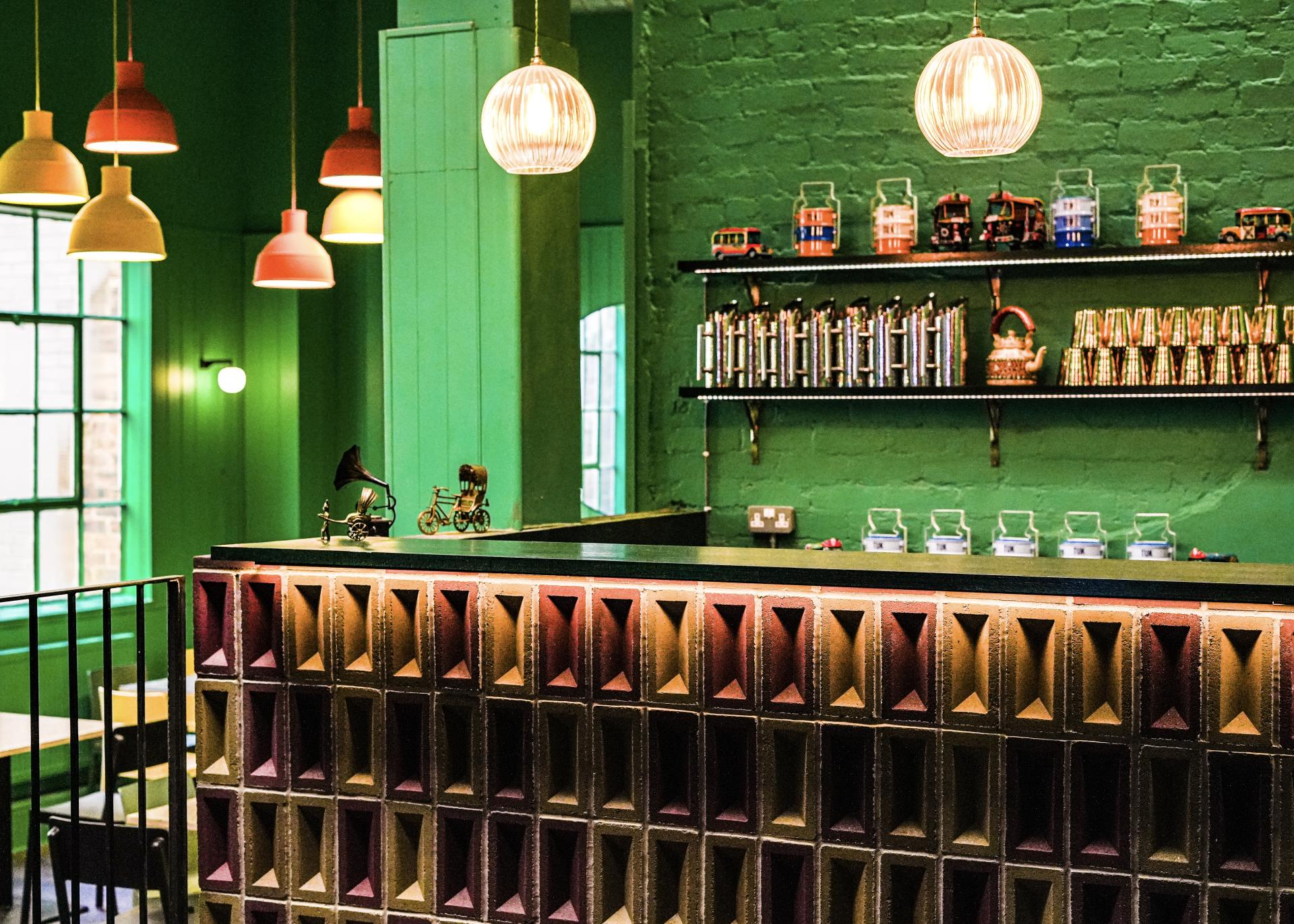 Colorful interior of a cafe featuring a unique brick counter, green walls, and vintage decor elements showcasing sustainable design.