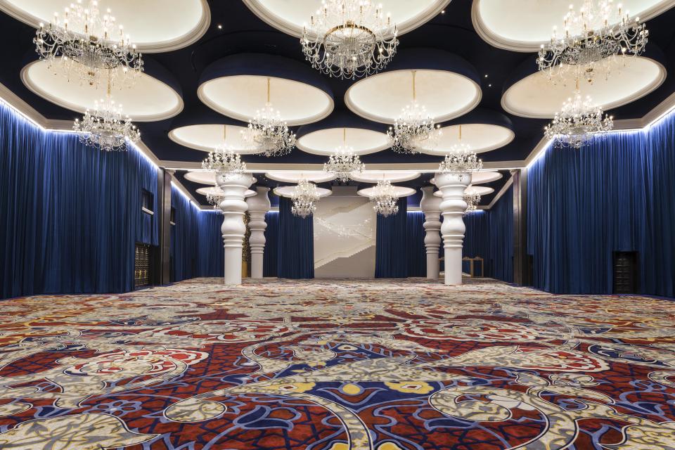 Luxurious ballroom interior at Mondrian Doha featuring ornate chandeliers, vibrant patterned carpet, and elegant blue drapery.