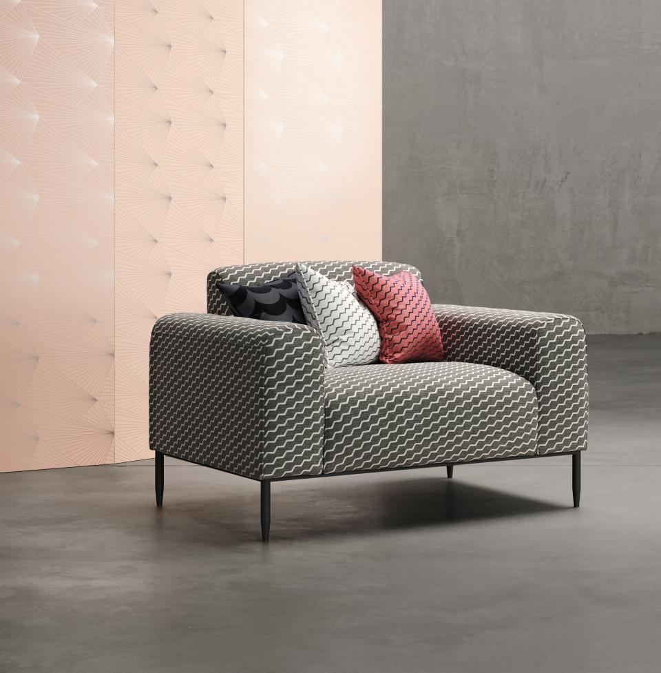 Modern Flock collaboration features a stylish sofa with geometric patterned upholstery and colorful cushions against textured wallpaper.