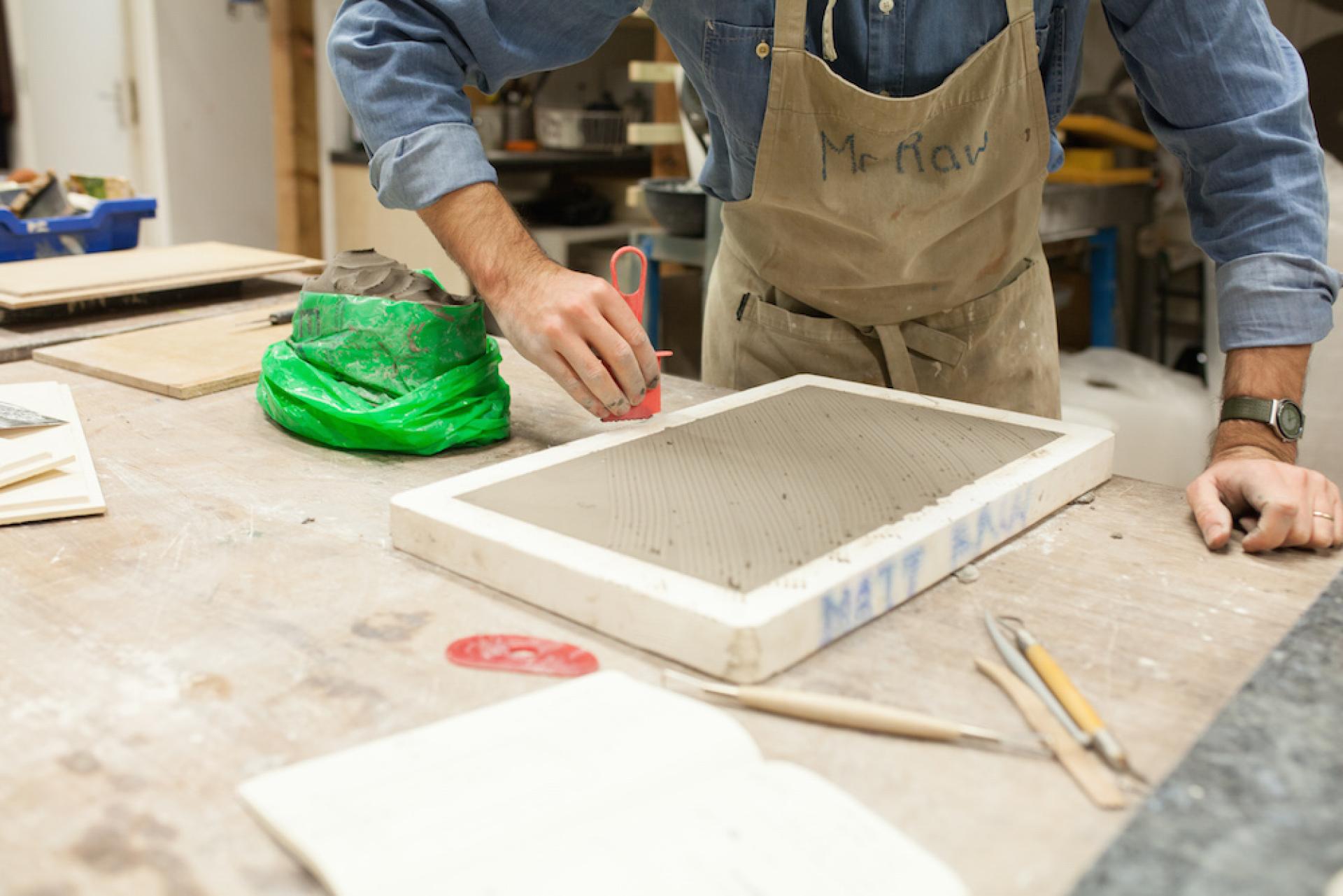 Ceramic artist Matthew Raw works with clay, using tools to create textured designs on a slab of wet clay.