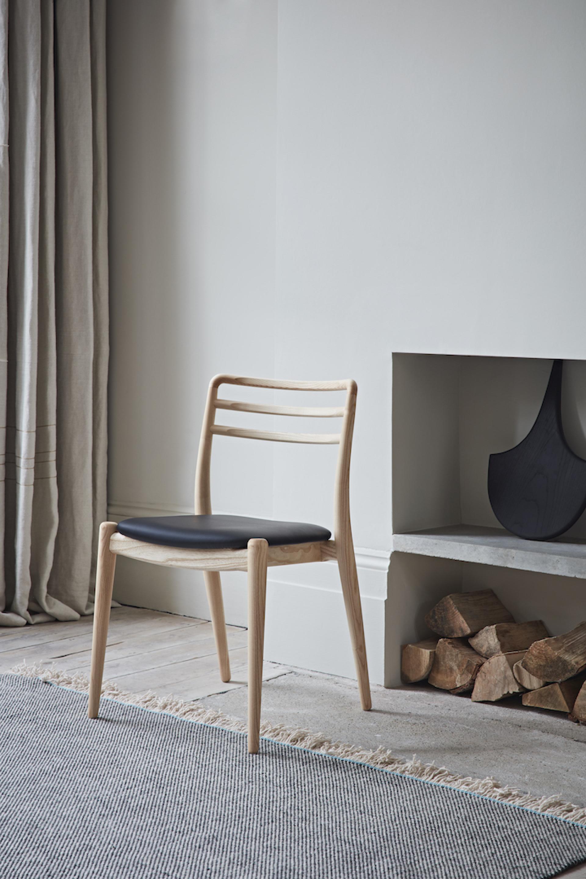Stylish wooden chair with a black seat, set in a minimalist living space showcasing British craftsmanship.