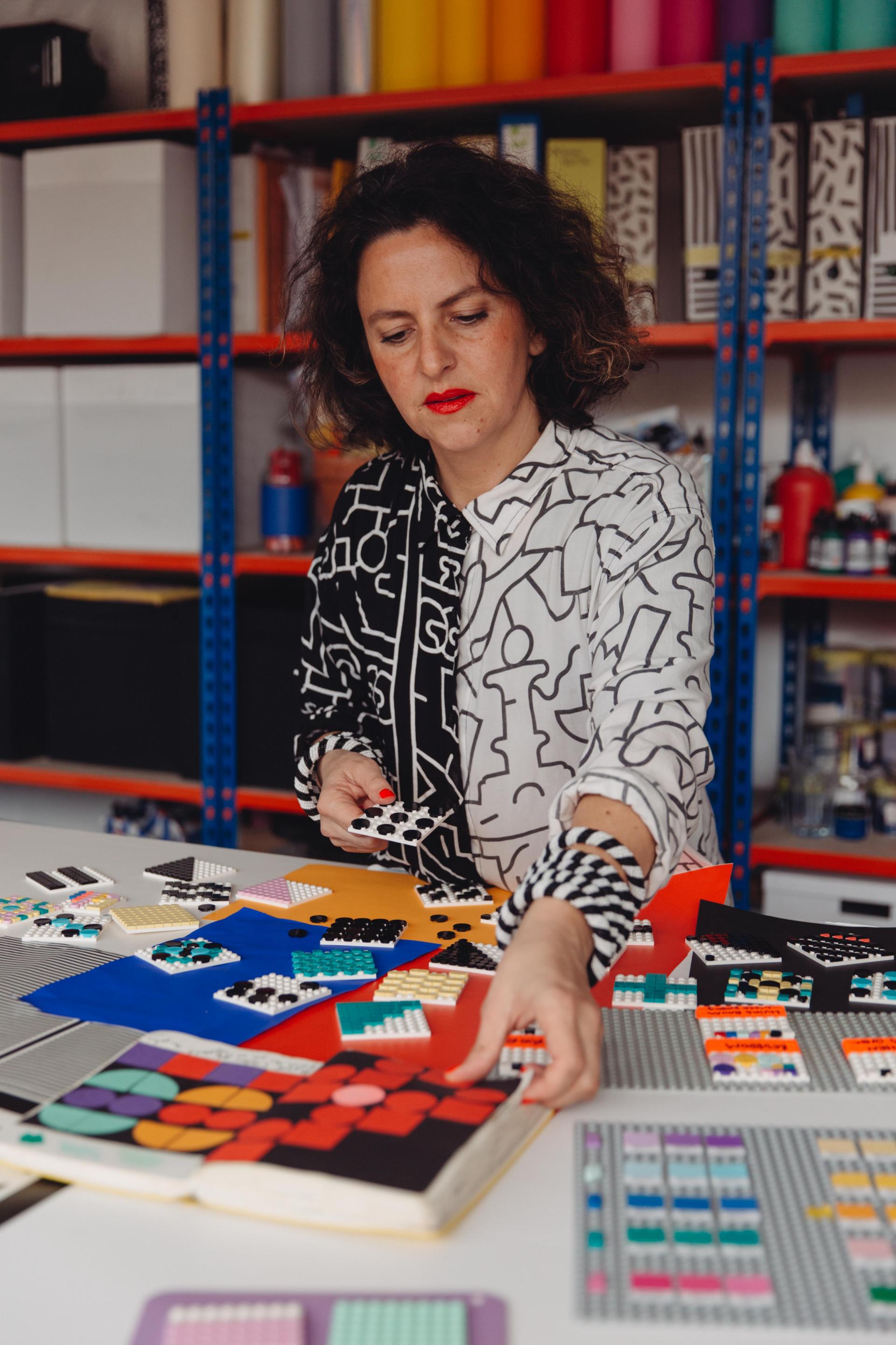 Camille Walala designs colorful LEGO patterns on a table, showcasing creativity for the HOUSE OF DOTS installation.