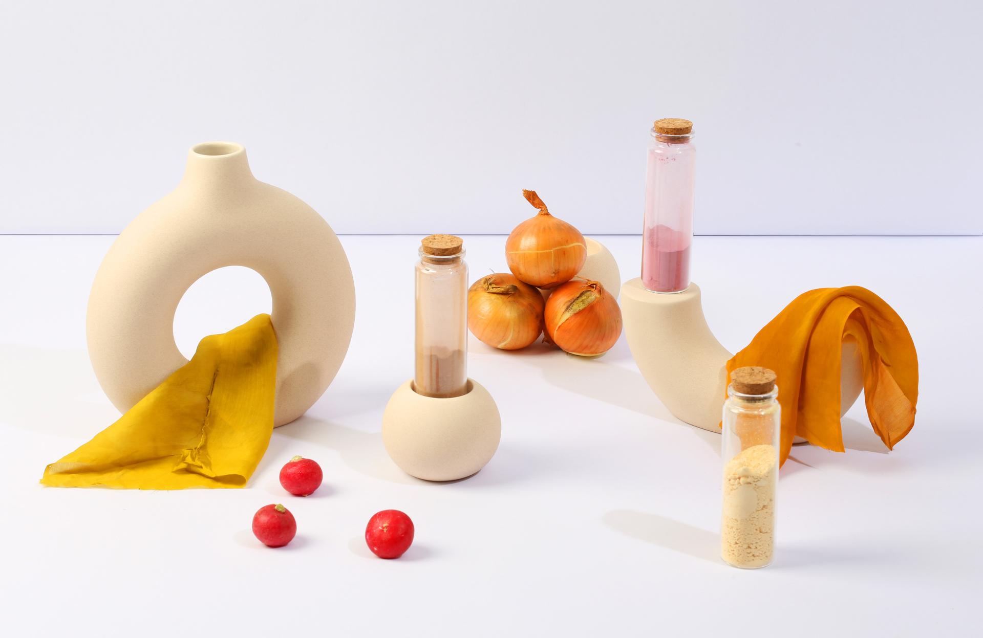 Contemporary vases and spice containers made from waste-based materials, surrounded by fresh produce, emphasizing regenerative design.