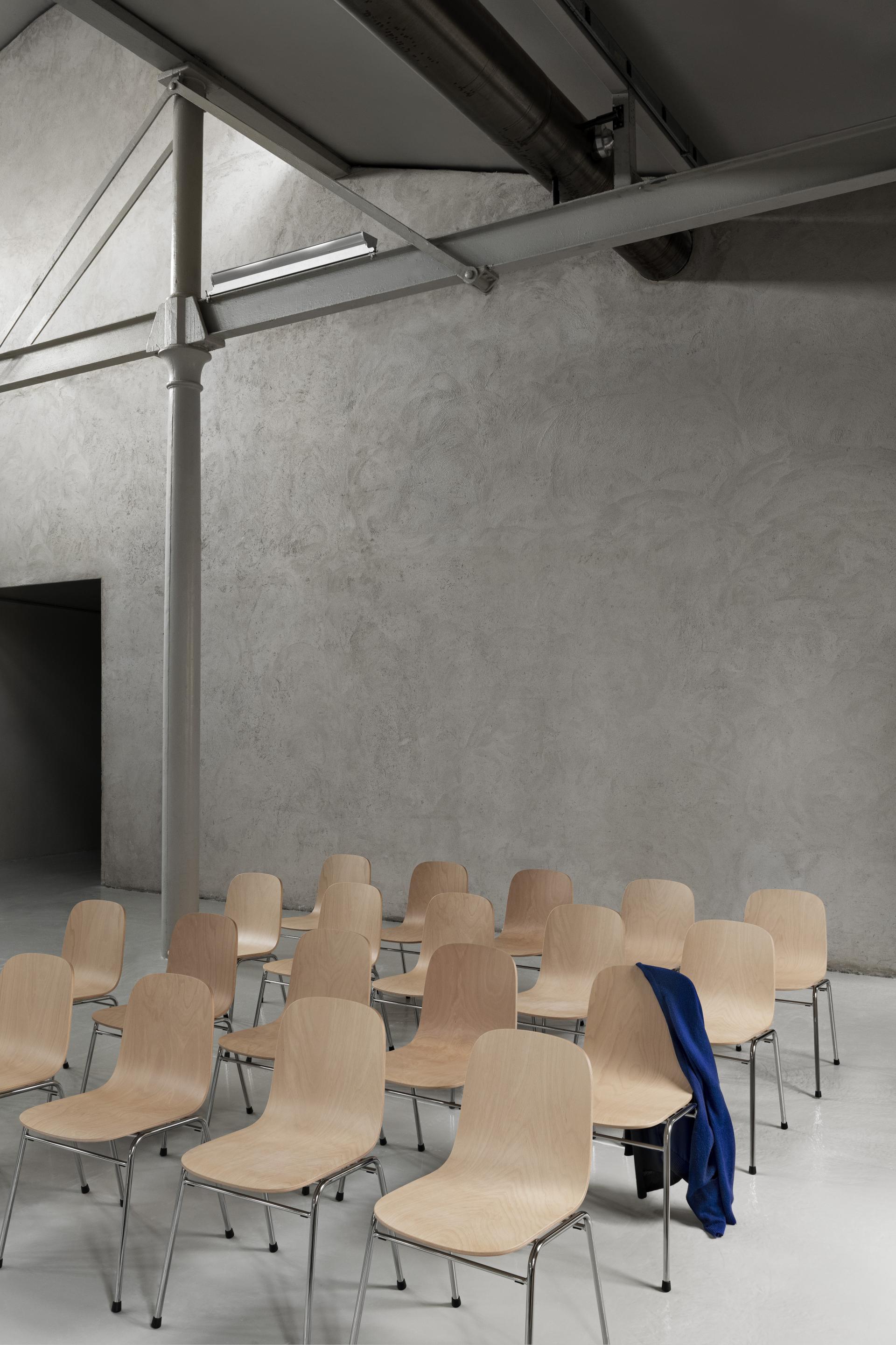 Minimalist seating arrangement featuring multiple Touchwood Chairs by Hem, set against a textured concrete wall.