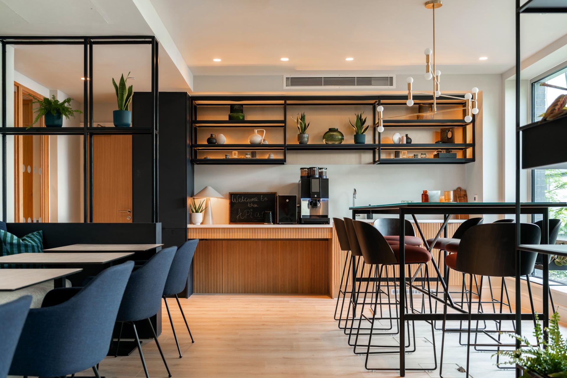 Modern co-living communal kitchen featuring stylish seating, shelves with decor, and a welcoming coffee station at The Apiary.