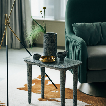 Decorative terrazzo table featuring a vase with greenery, bowls, and a gold dish, against a stylish interior backdrop.