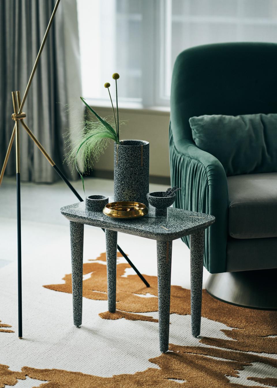 Decorative terrazzo table featuring a vase with greenery, bowls, and a gold dish, against a stylish interior backdrop.