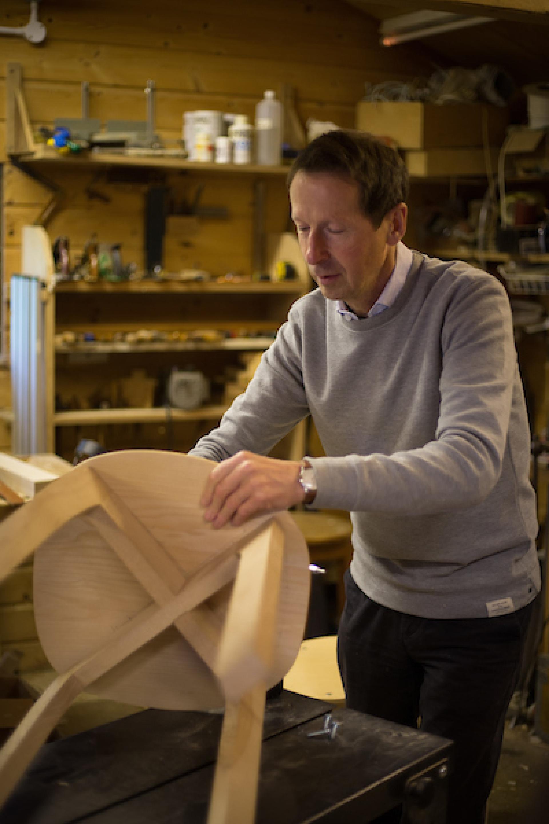 Craftsman shaping a wooden chair in a workshop, reflecting modern Scandinavian design techniques and craftsmanship.