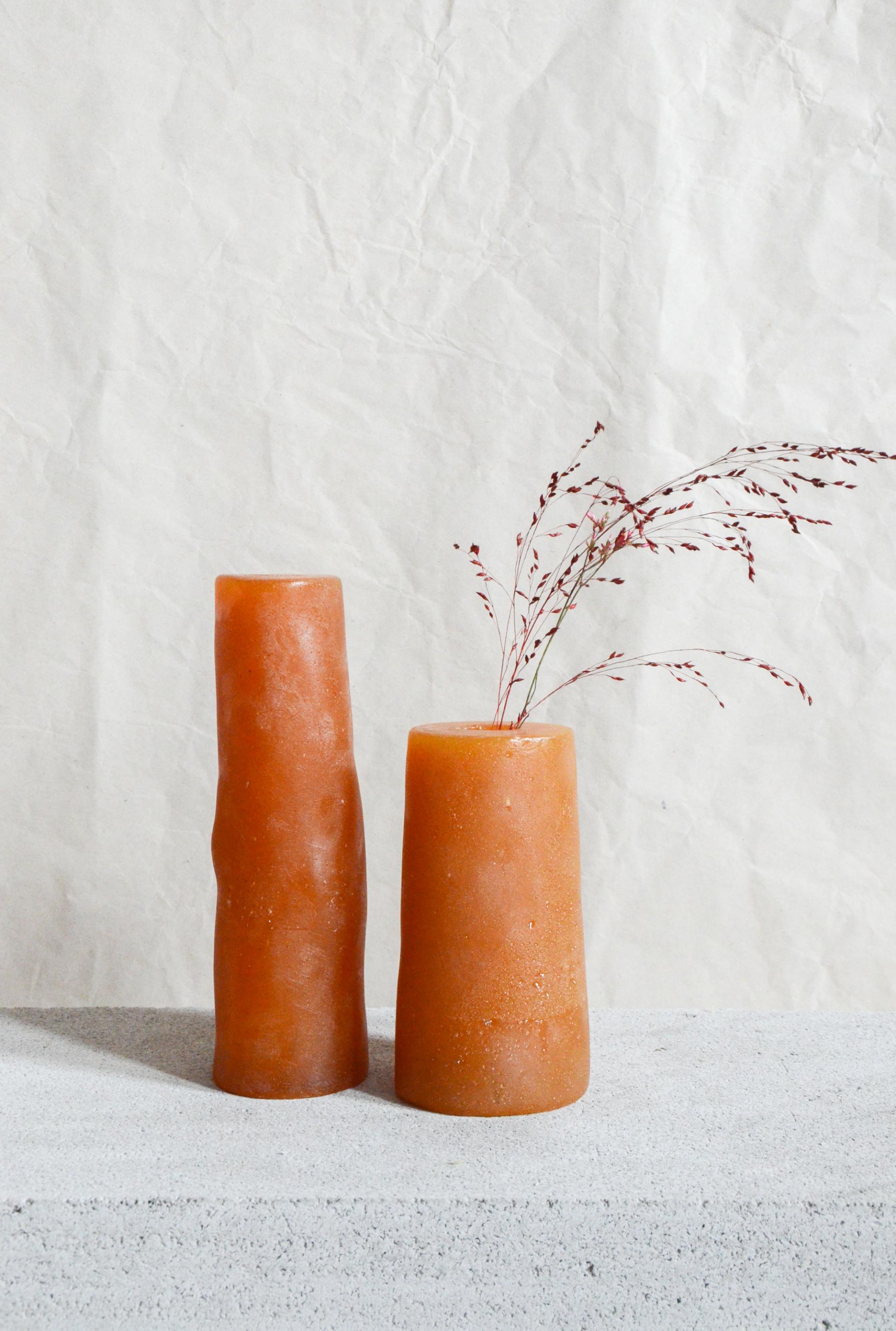 Unique sculptural biomaterial vases made from orange resin, beautifully complemented with dried grass accents against a textured background.