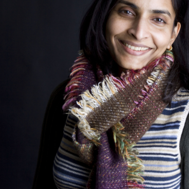 Vanika Lath smiling in a striped sweater and colorful scarf, representing innovation and sustainability at Sensitile Systems.