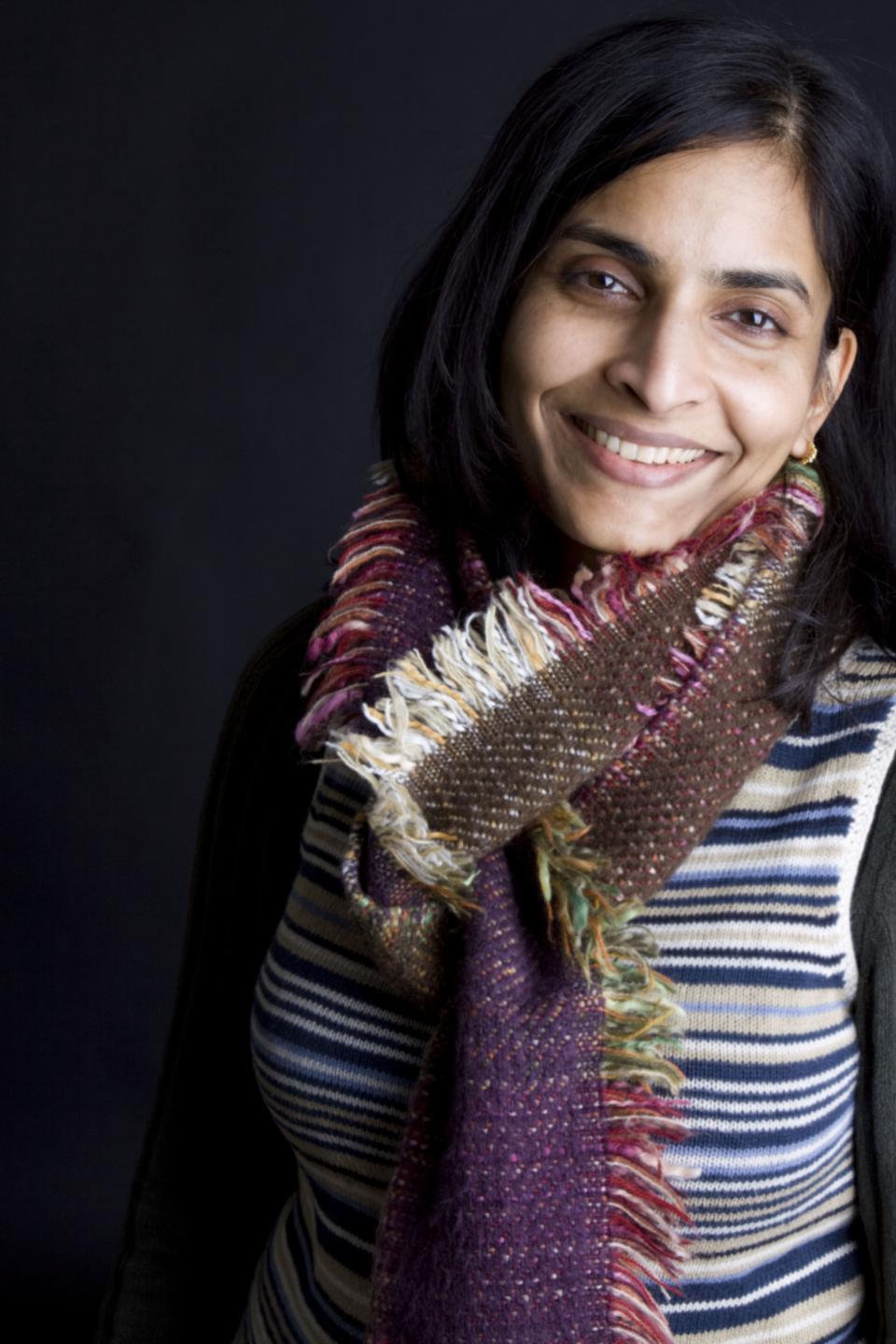 Vanika Lath smiling in a striped sweater and colorful scarf, representing innovation and sustainability at Sensitile Systems.