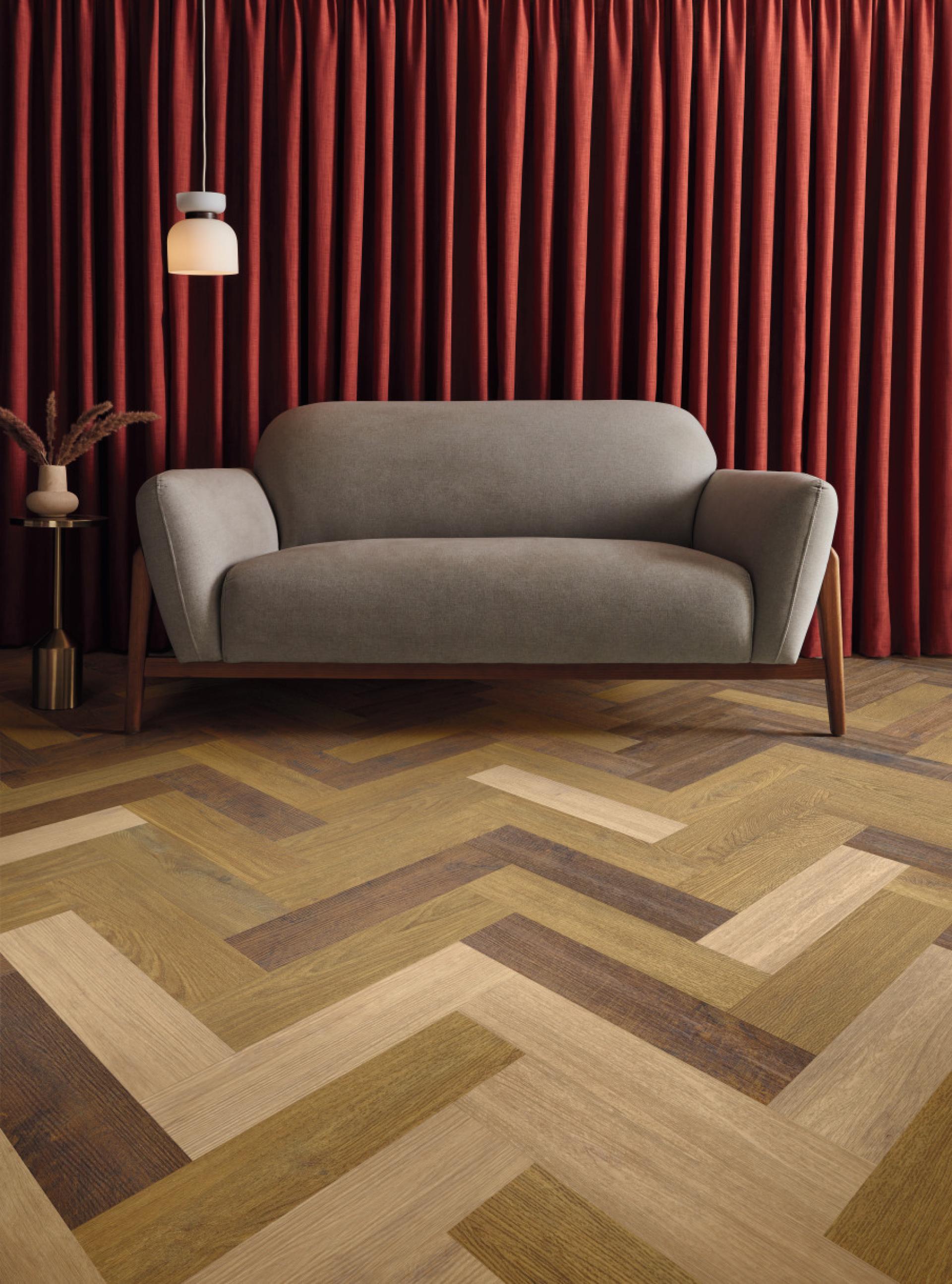 Stylish oak herringbone flooring complements a modern living space with a grey sofa and rich red curtains.