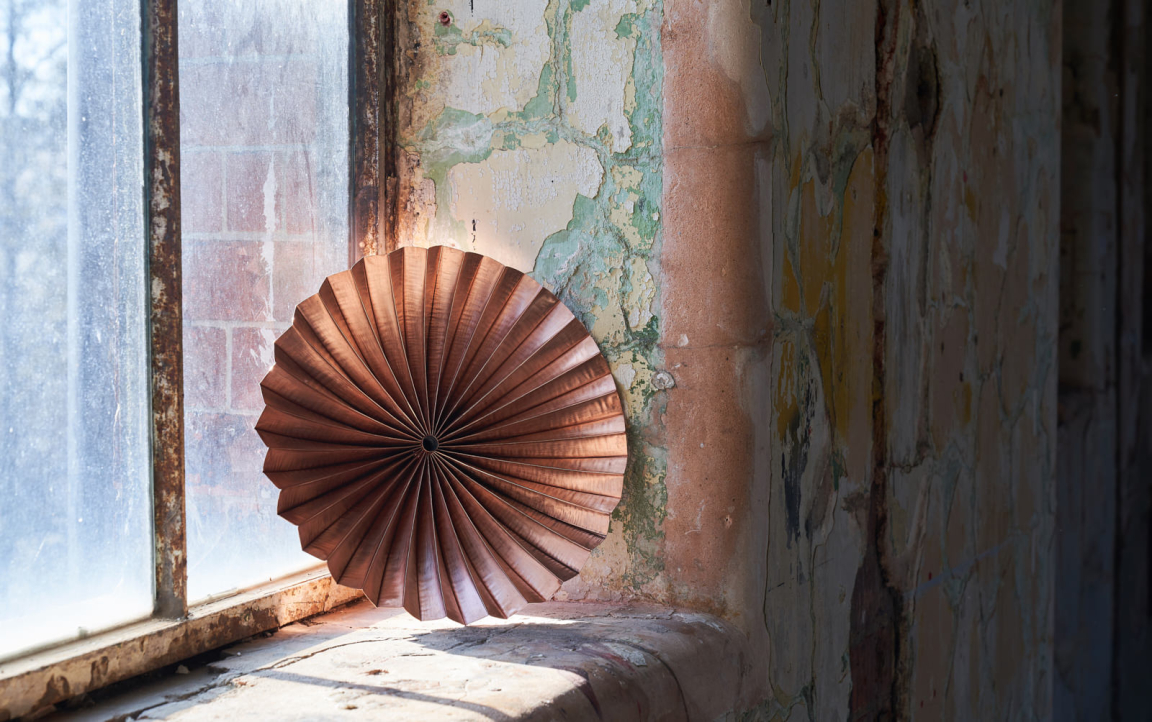 Wooden circular sculpture showcased on a windowsill in an industrial space, highlighting innovative craft design.