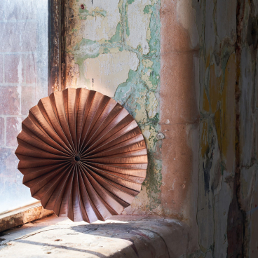 Wooden circular sculpture showcased on a windowsill in an industrial space, highlighting innovative craft design.