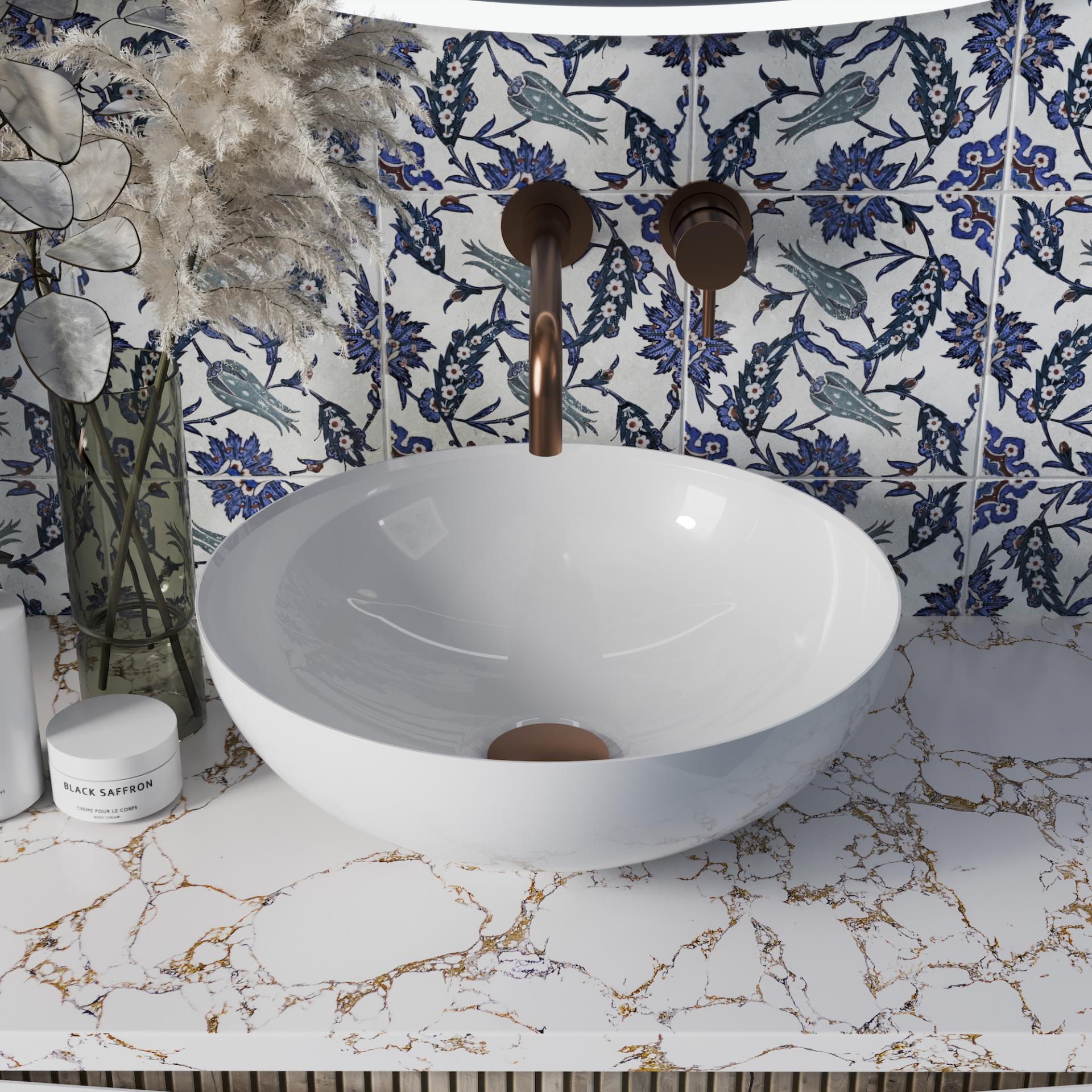 Elegant white basin with stylish bronze faucets, set against a patterned blue tiled wall in a modern washroom.