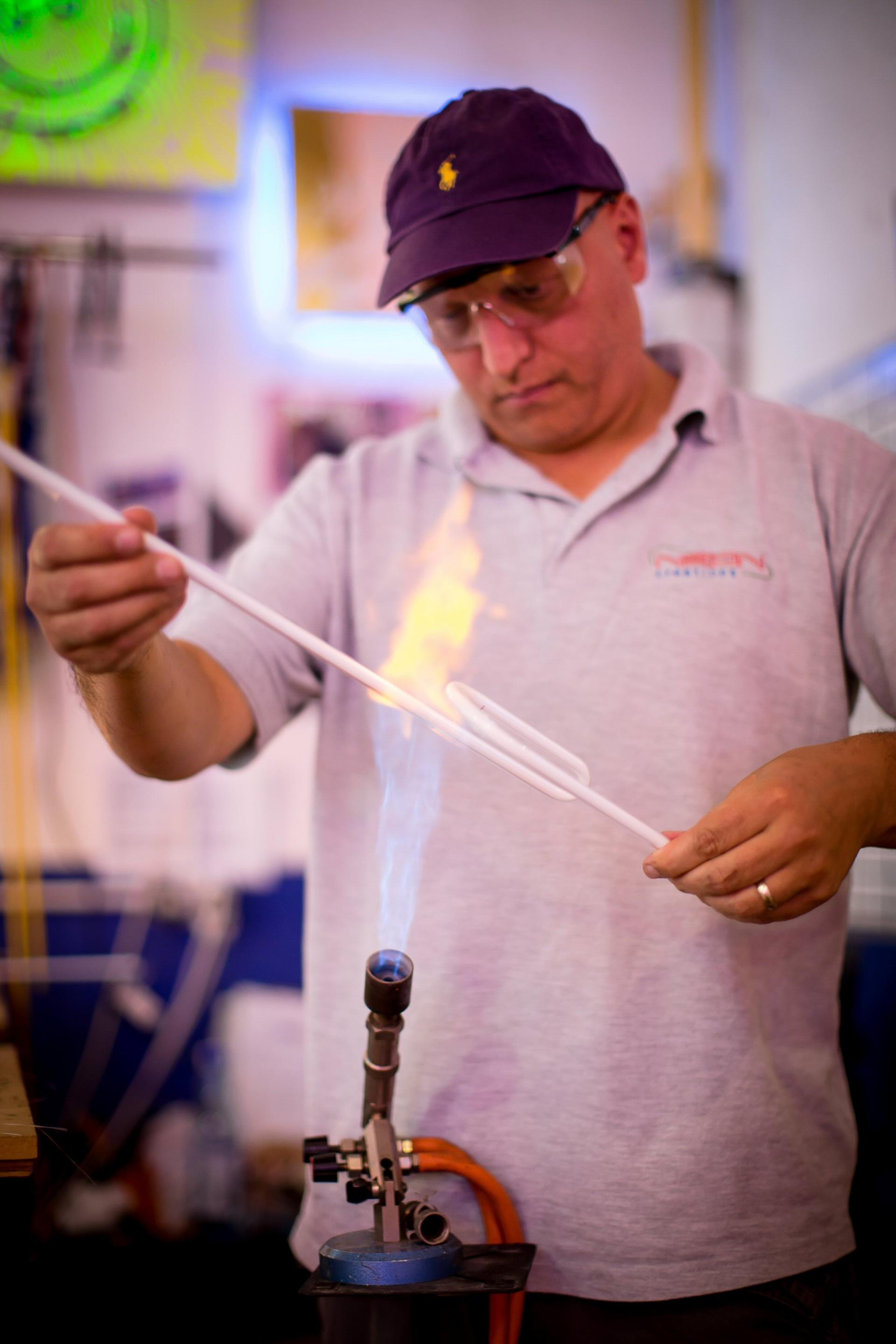 Craftsman shaping glass tubes for neon signs, using a flame torch in a vibrant workshop setting.