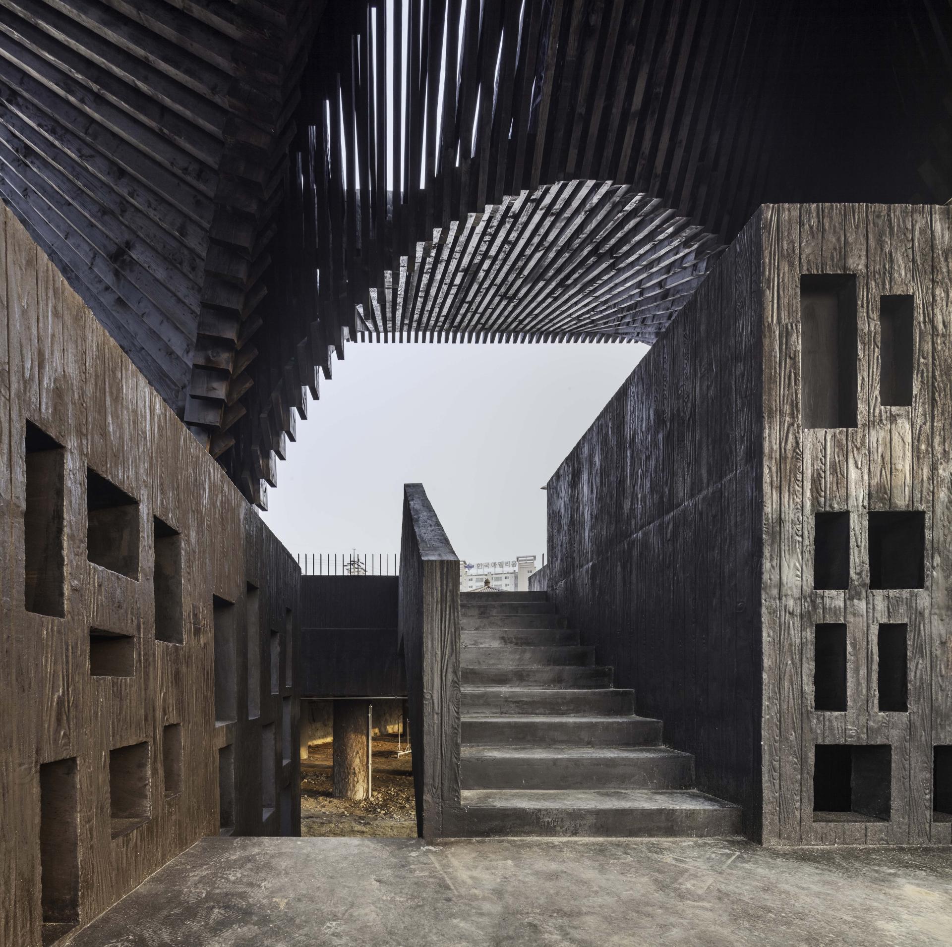 Monumental architecture features a staircase and textured walls, symbolizing memory and commemoration in David Adjaye's exhibition.