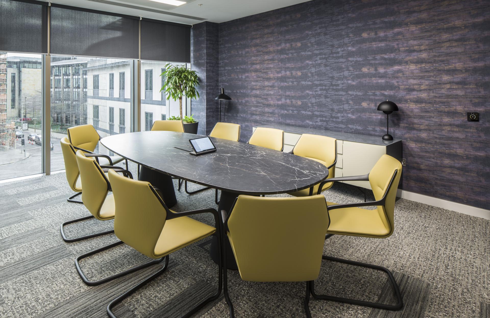 Modern conference room with a large oval table, yellow chairs, and ample natural light, showcasing a WELL-certified office design.