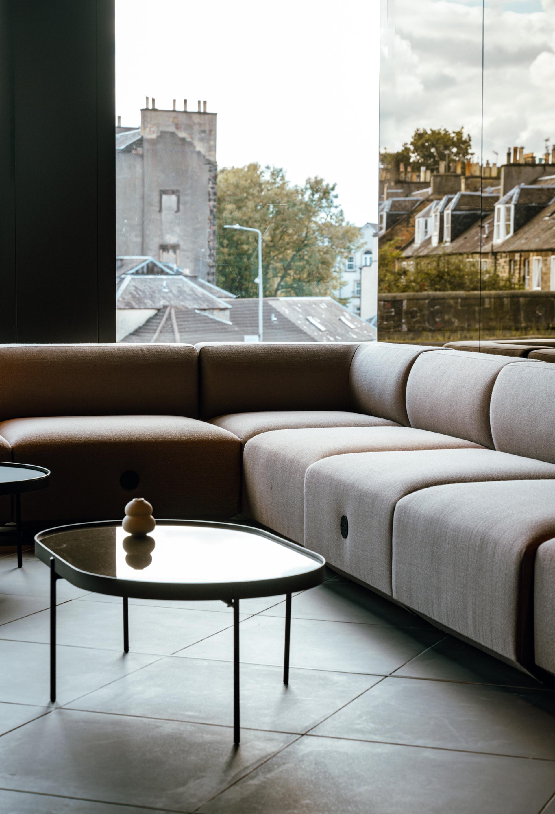 Contemporary lounge area featuring a modern, curved sofa and sleek coffee table in Dentons' Edinburgh workspace.