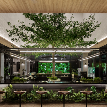 A modern restaurant interior featuring a central tree, vibrant greenery, and a sleek bar design, embodying nature-themed artistry.