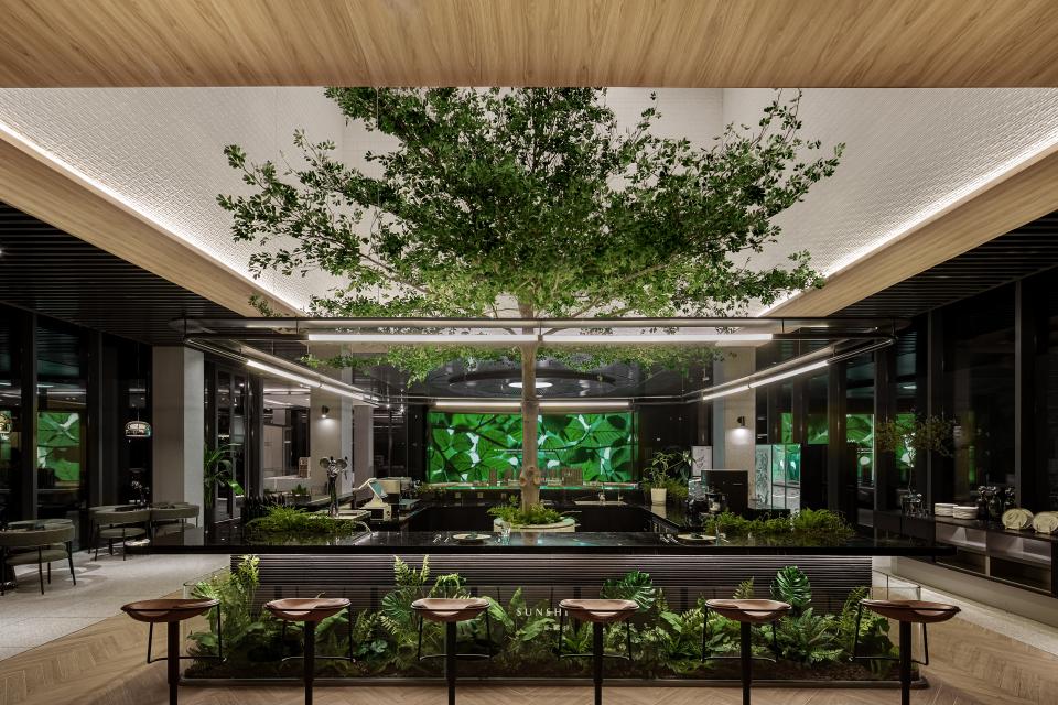 A modern restaurant interior featuring a central tree, vibrant greenery, and a sleek bar design, embodying nature-themed artistry.