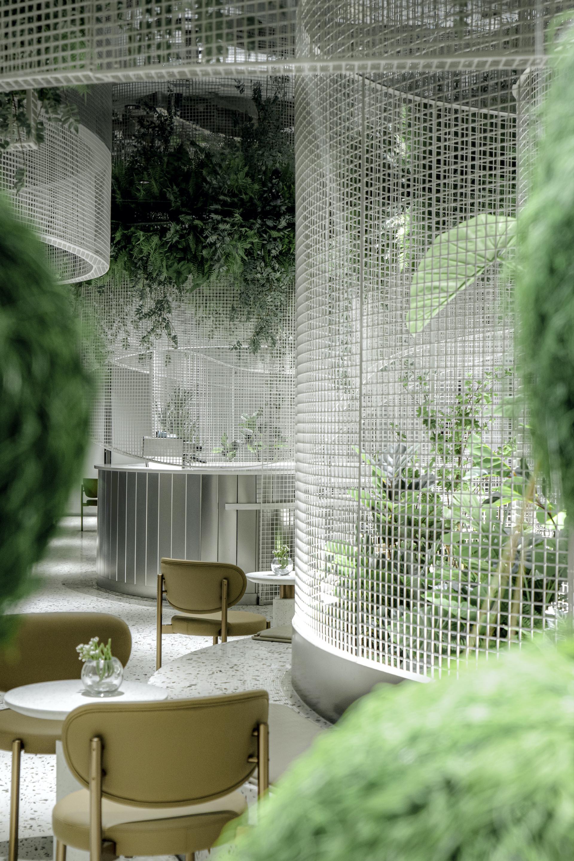 Stylish café interior featuring terrazzo flooring, curved mesh grids, and lush greenery designed by Karv One.