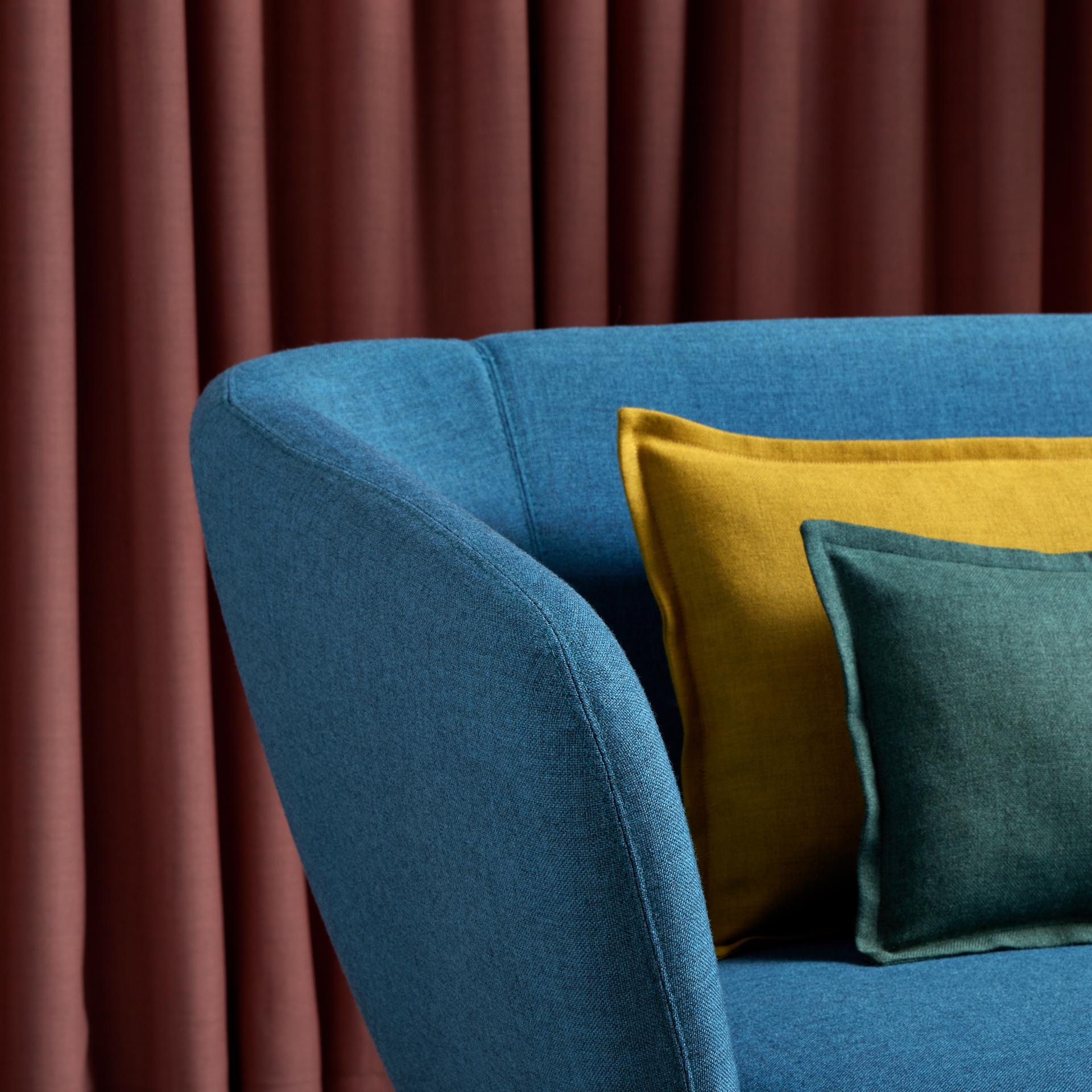 Stylish blue chair with vibrant cushions in green and mustard, showcasing Camira's expanded Sumi wool fabric colors.