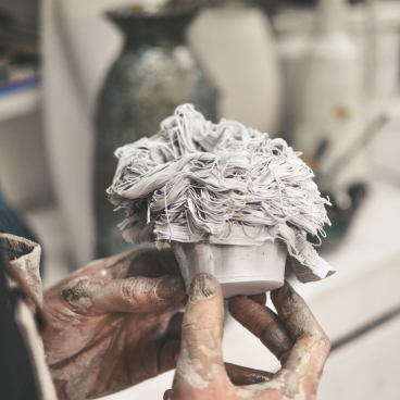 Artisan holding a small ceramic sculpture with a textured, abstract design, representing creativity and inspiration in 2021.