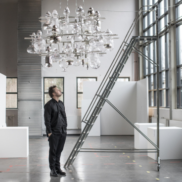 A man gazes at an intricate glass chandelier in the spacious Glass Factory in Småland, showcasing creativity.