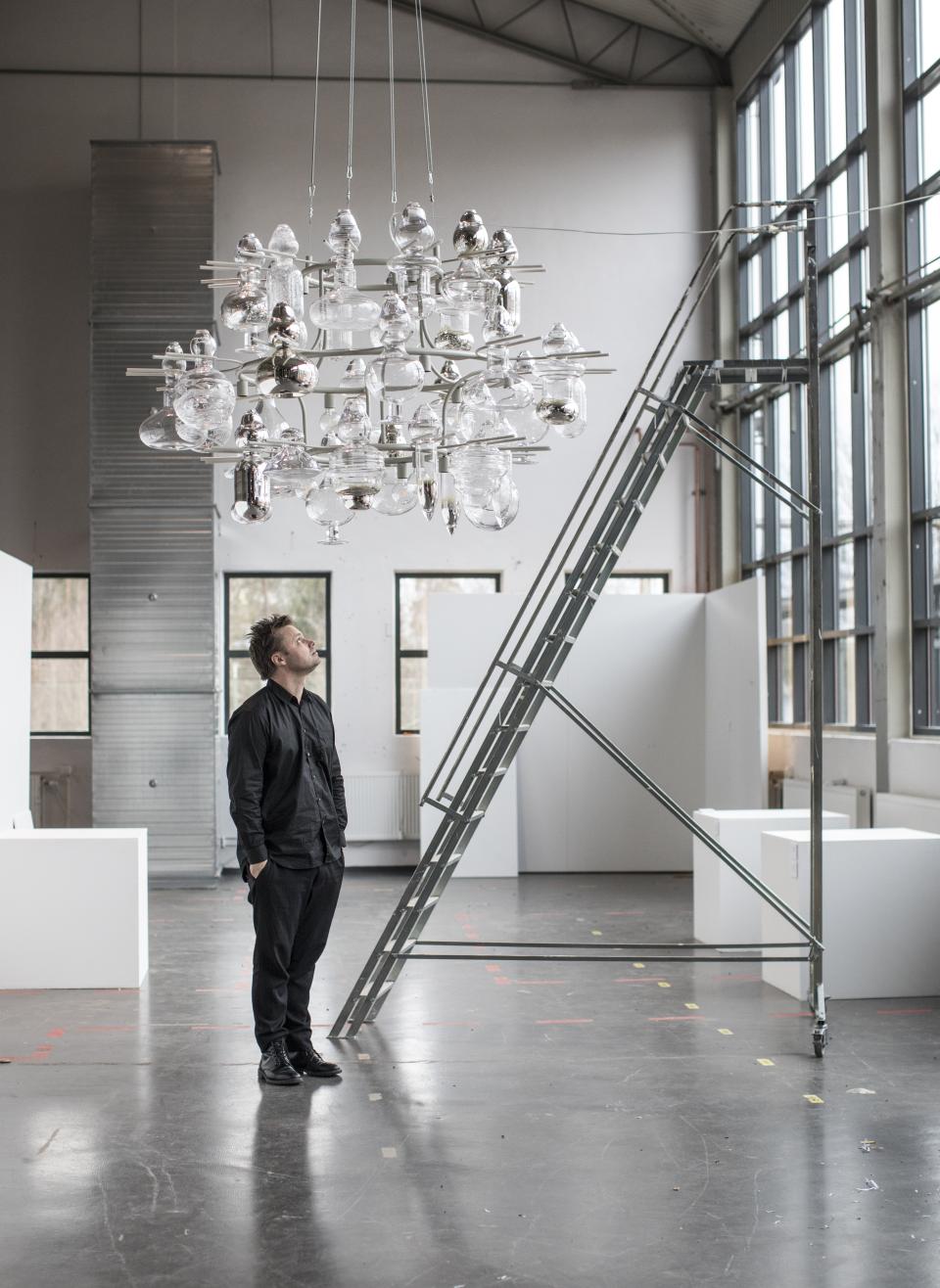 A man gazes at an intricate glass chandelier in the spacious Glass Factory in Småland, showcasing creativity.