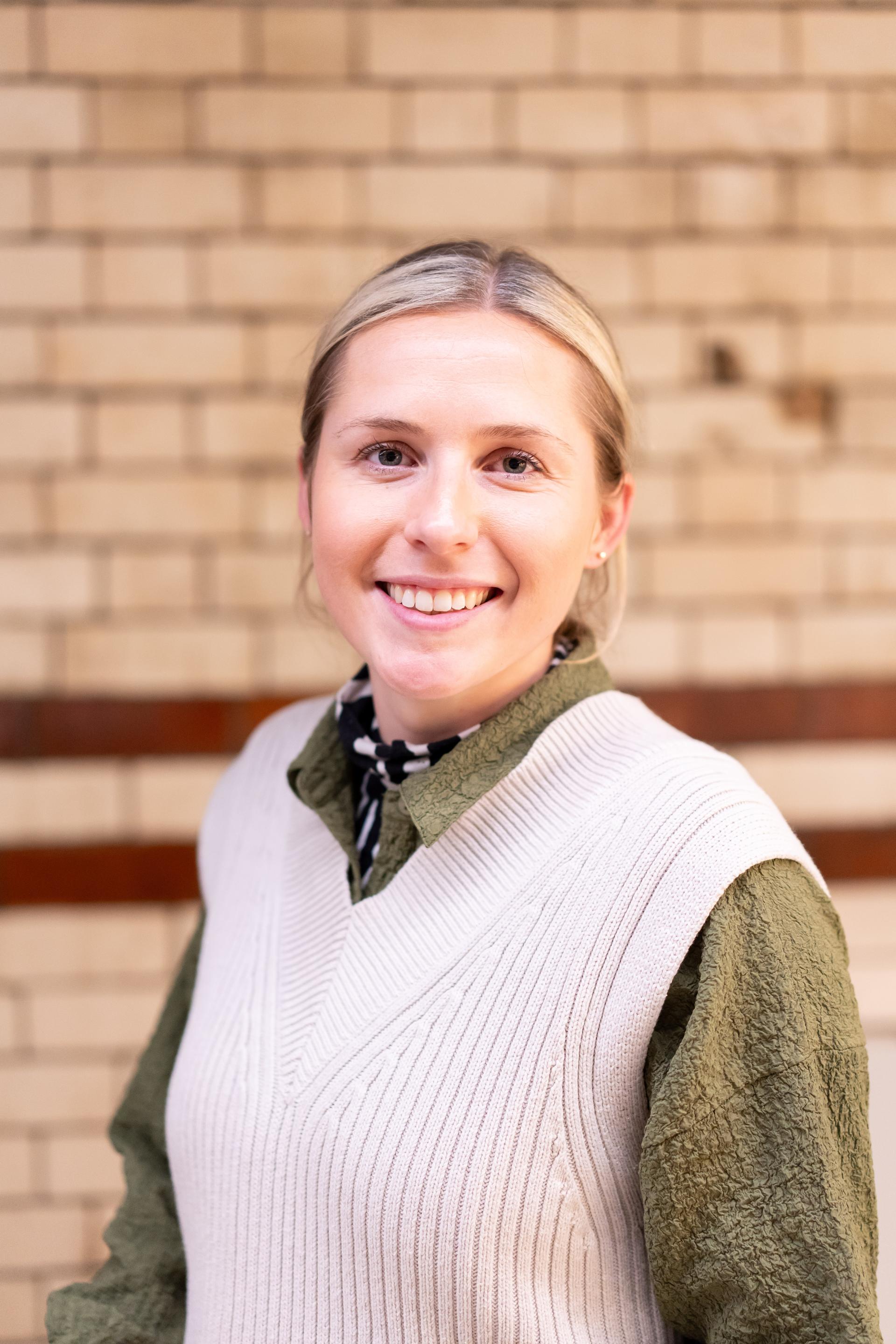 Smiling woman in a knitted sweater poses against a brick wall, embodying themes of EDI and inclusive culture.