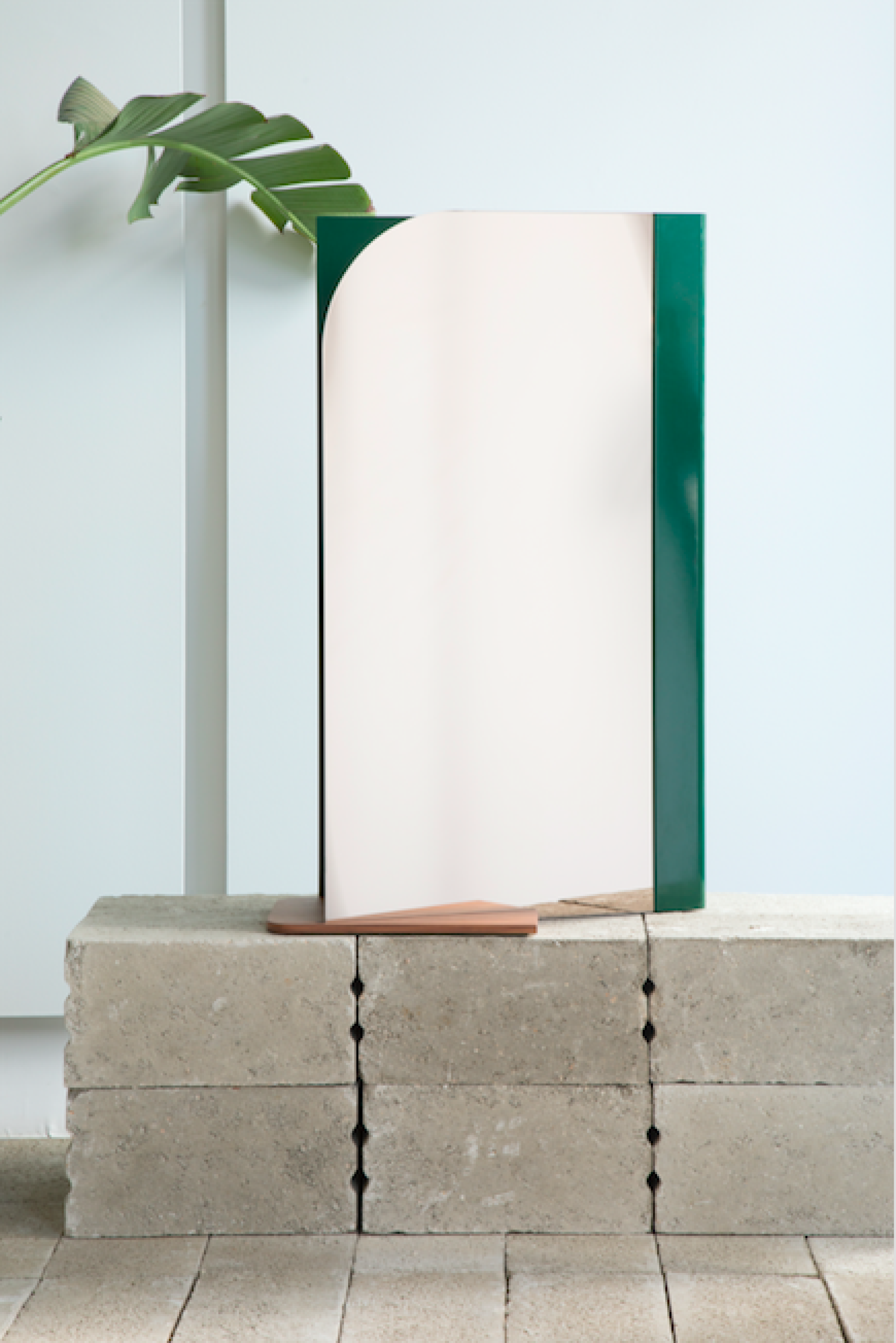 Stylish geometric mirror with a green border and pink surface, displayed on concrete blocks, enhancing modern interior design.
