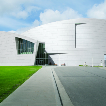 Modern architectural building featuring Hanex® Solid Surface material, surrounded by landscaped green space under a partly cloudy sky.