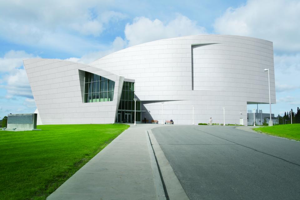 Modern architectural building featuring Hanex® Solid Surface material, surrounded by landscaped green space under a partly cloudy sky.