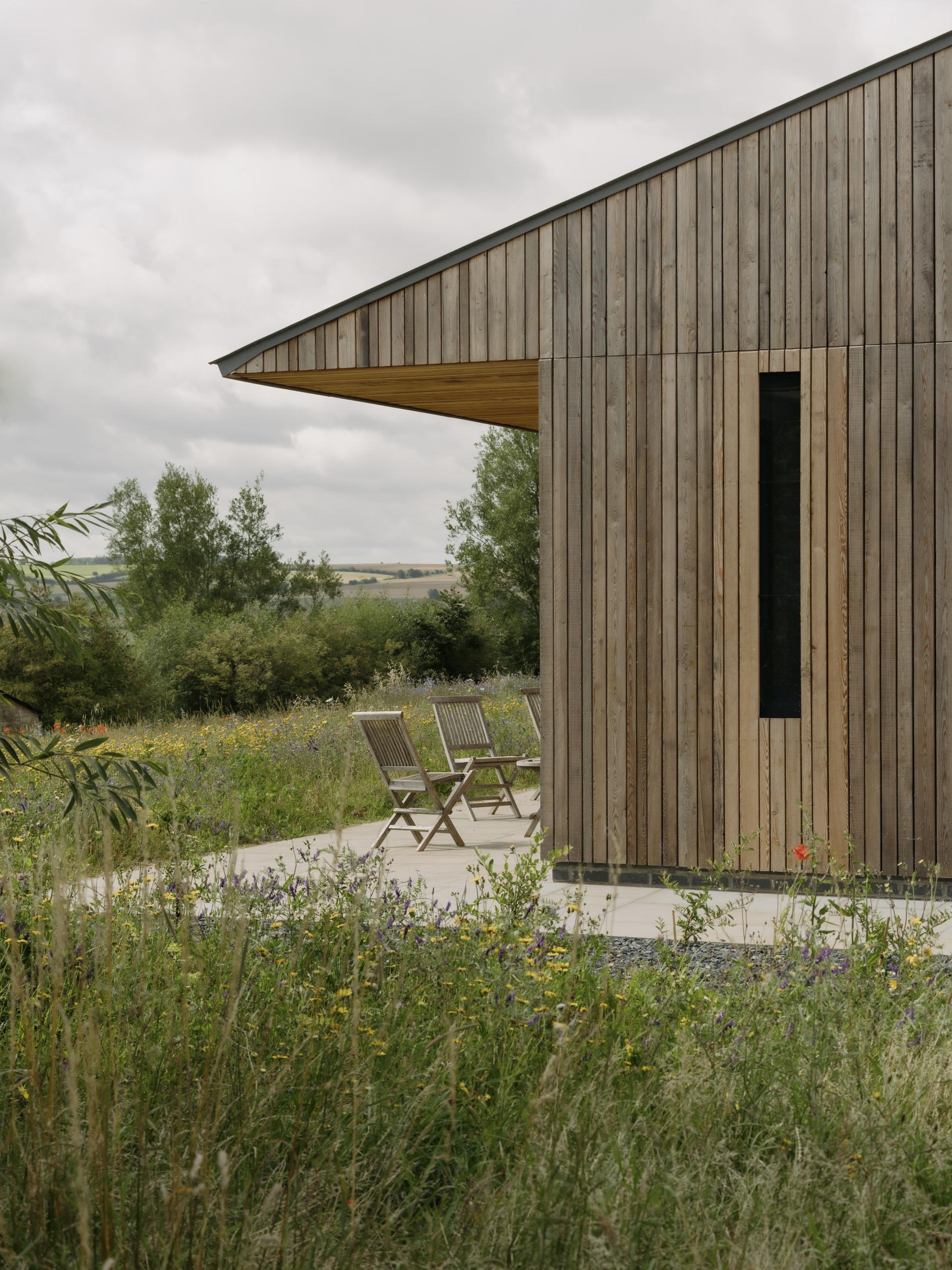 Sustainable farming education centre designed by Timothy Tasker Architects, featuring a wooden exterior and surrounded by wildflowers.