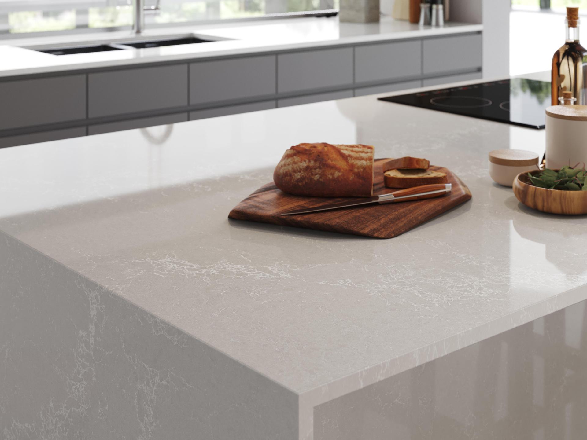 Caesarstone's Alpine Mist surface showcased in a modern kitchen with bread and snacks on a wooden cutting board.