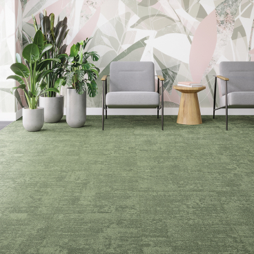 Modern workspace featuring green Tessera Infused carpet tiles, sleek gray seating, decorative plants, and a stylish wooden table.