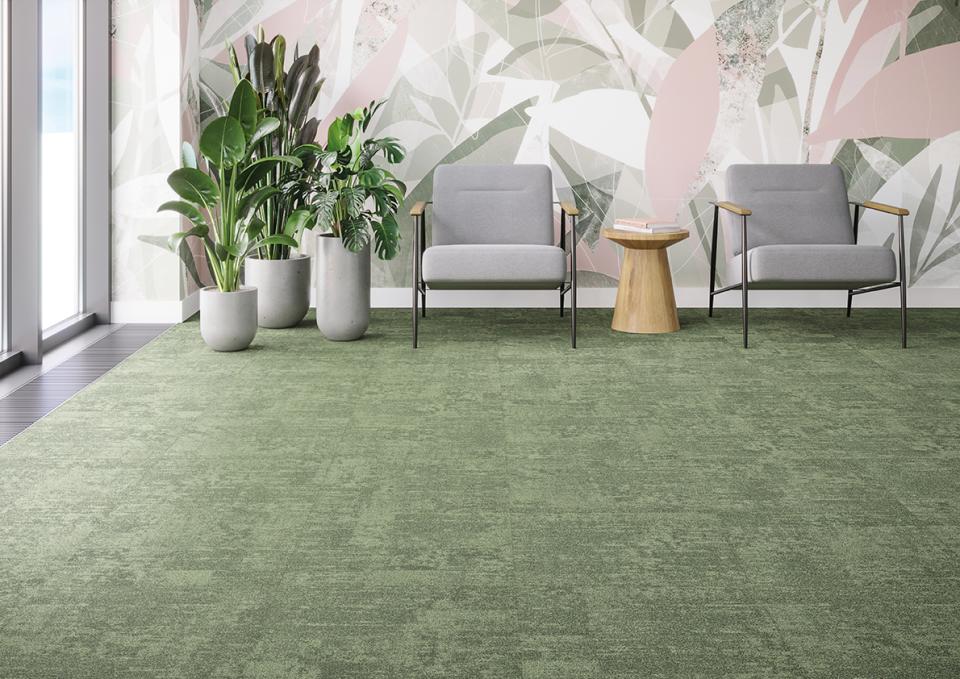 Modern workspace featuring green Tessera Infused carpet tiles, sleek gray seating, decorative plants, and a stylish wooden table.