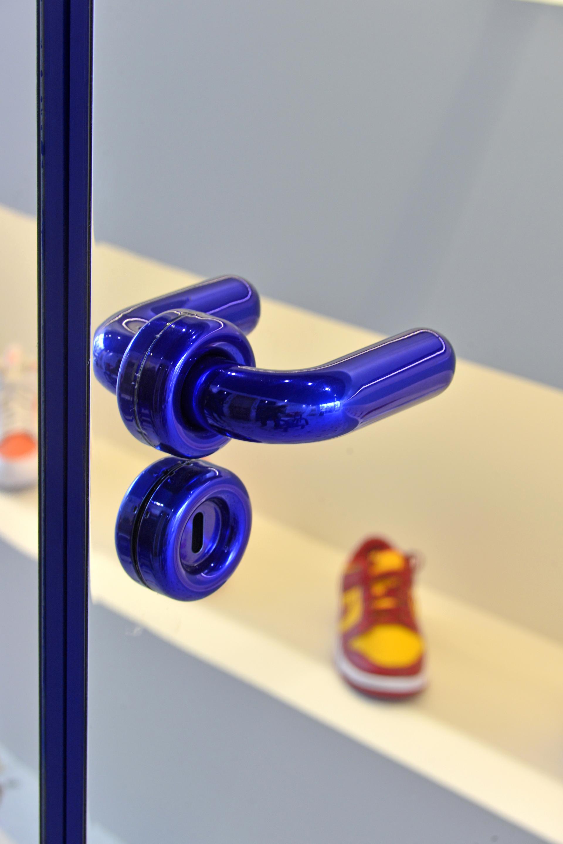 Sleek electric blue door handle in Brudey Sneakers concept store, showcasing modern design alongside vibrant sneaker display.