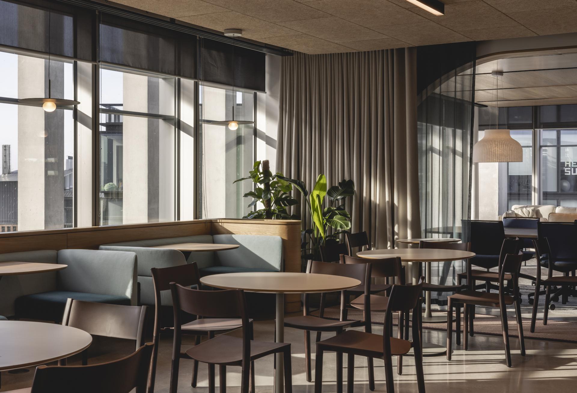 Bright and modern workspace designed by Ekho Studio for AstraZeneca, featuring seating, plants, and large windows.