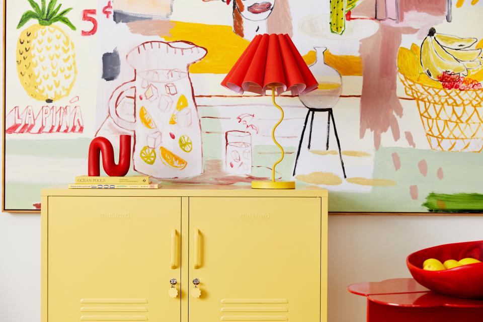 Bright yellow cabinet with a red lamp, surrounded by colorful artwork and vibrant decor reflecting Mustard Made's new Butter shade.