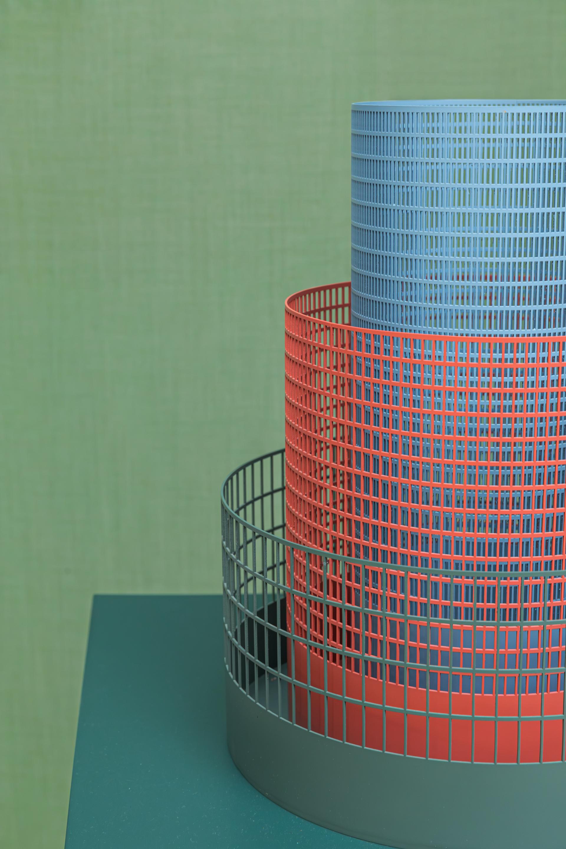 Stacked bio-based color palettes in red and blue mesh baskets on a green background, showcasing innovative material design.