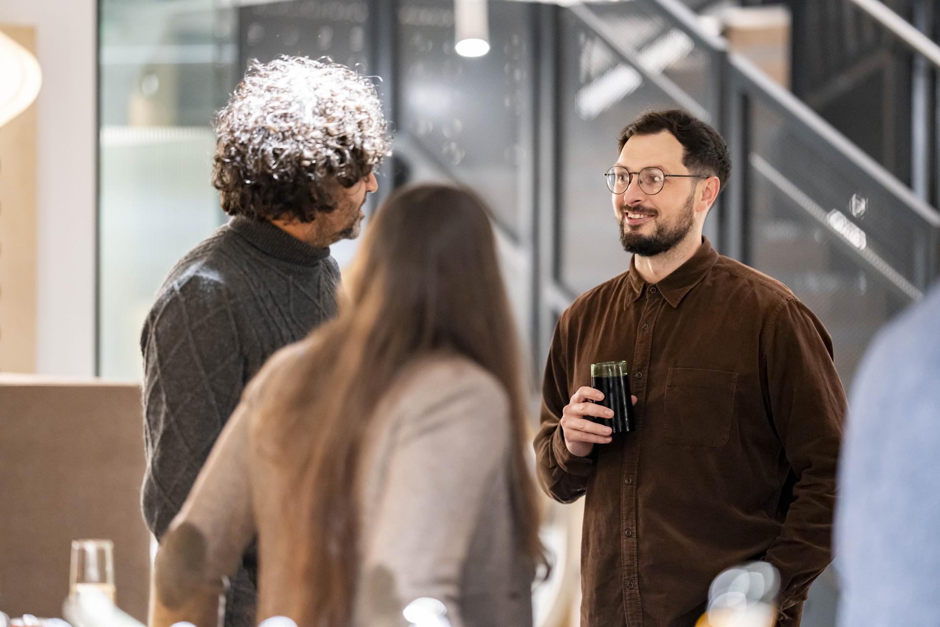 Colleagues engage in conversation at a modern workplace event, discussing technology's impact on work dynamics.
