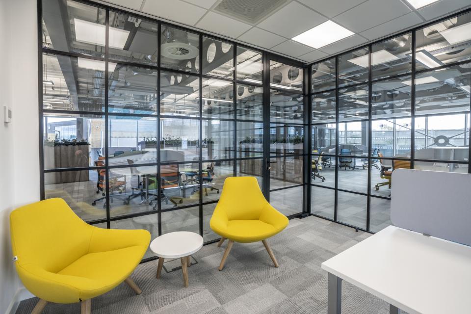 Bright yellow chairs and a small table in a modern office setting featuring flexible furniture design for enhanced workspace productivity.