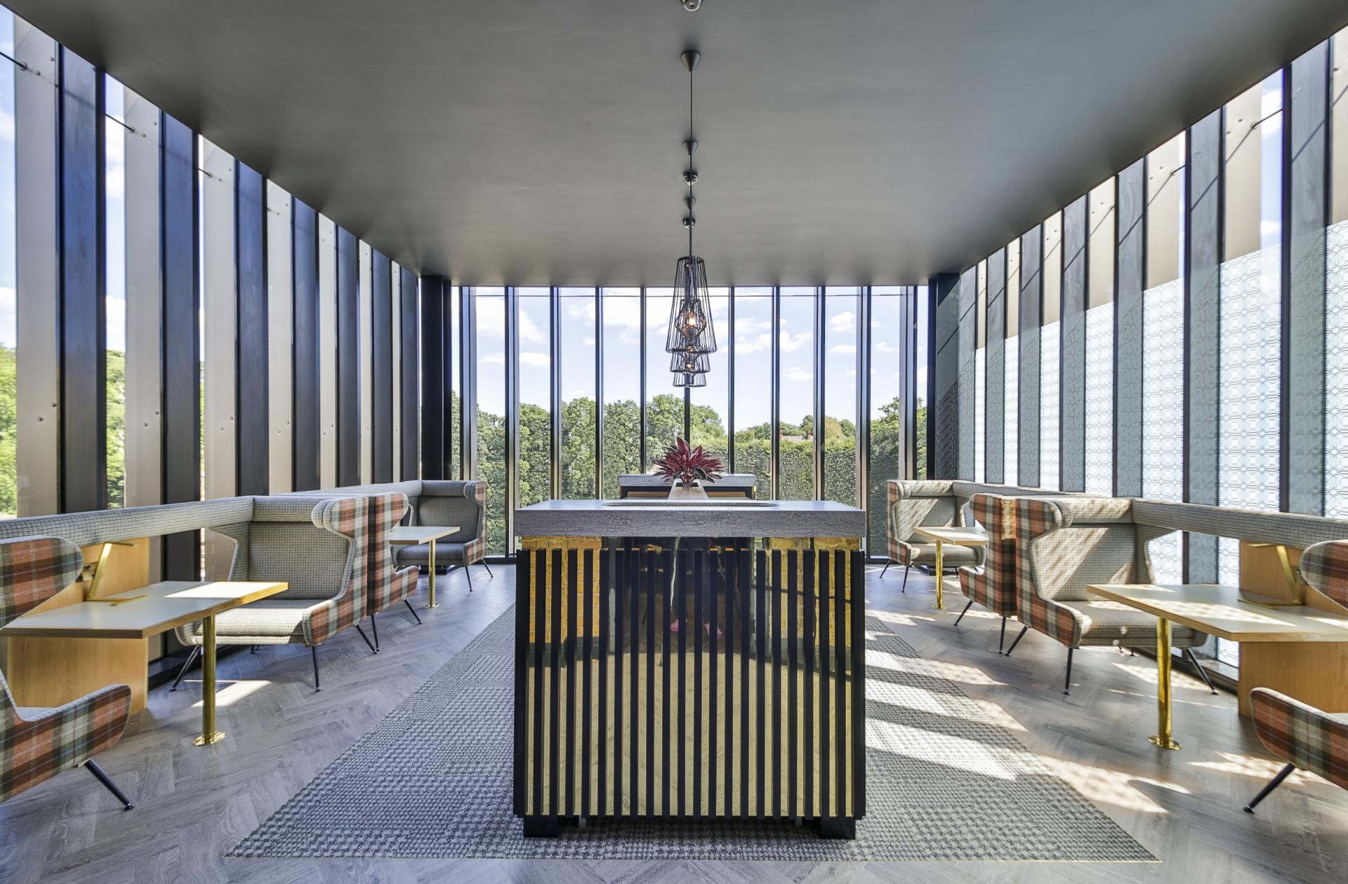 Contemporary interior design space featuring a stylish bar, patterned seating, and large windows overlooking greenery in Manchester.