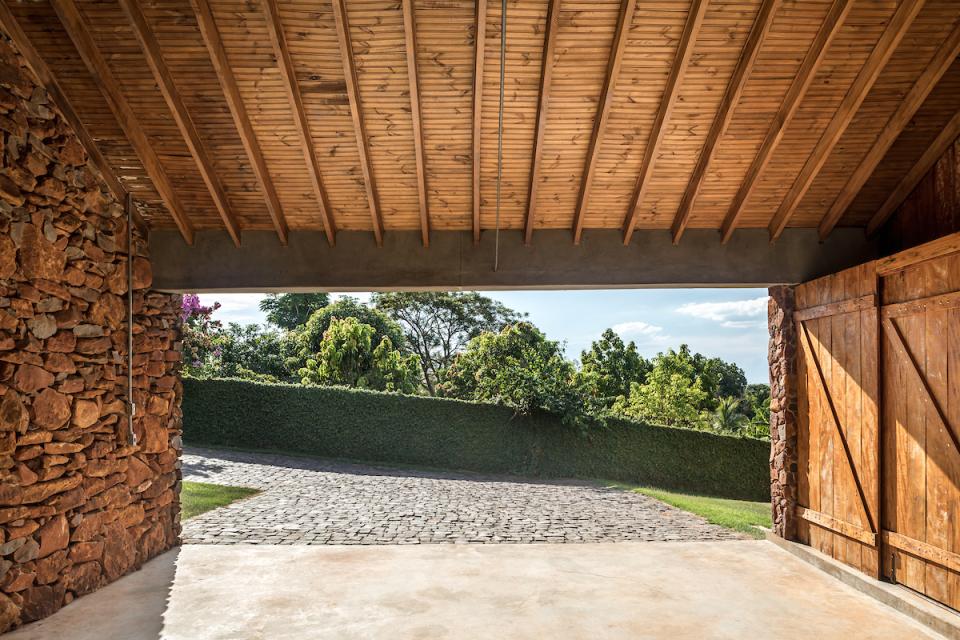 Interior view of The Lake House by Solo Arquitetos, showcasing natural stone walls and wooden beams with lush greenery outside.