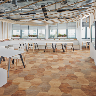 Modern workspace featuring hexagonal wood flooring, minimalist furniture, and abundant natural light emphasizing workplace hospitality design.