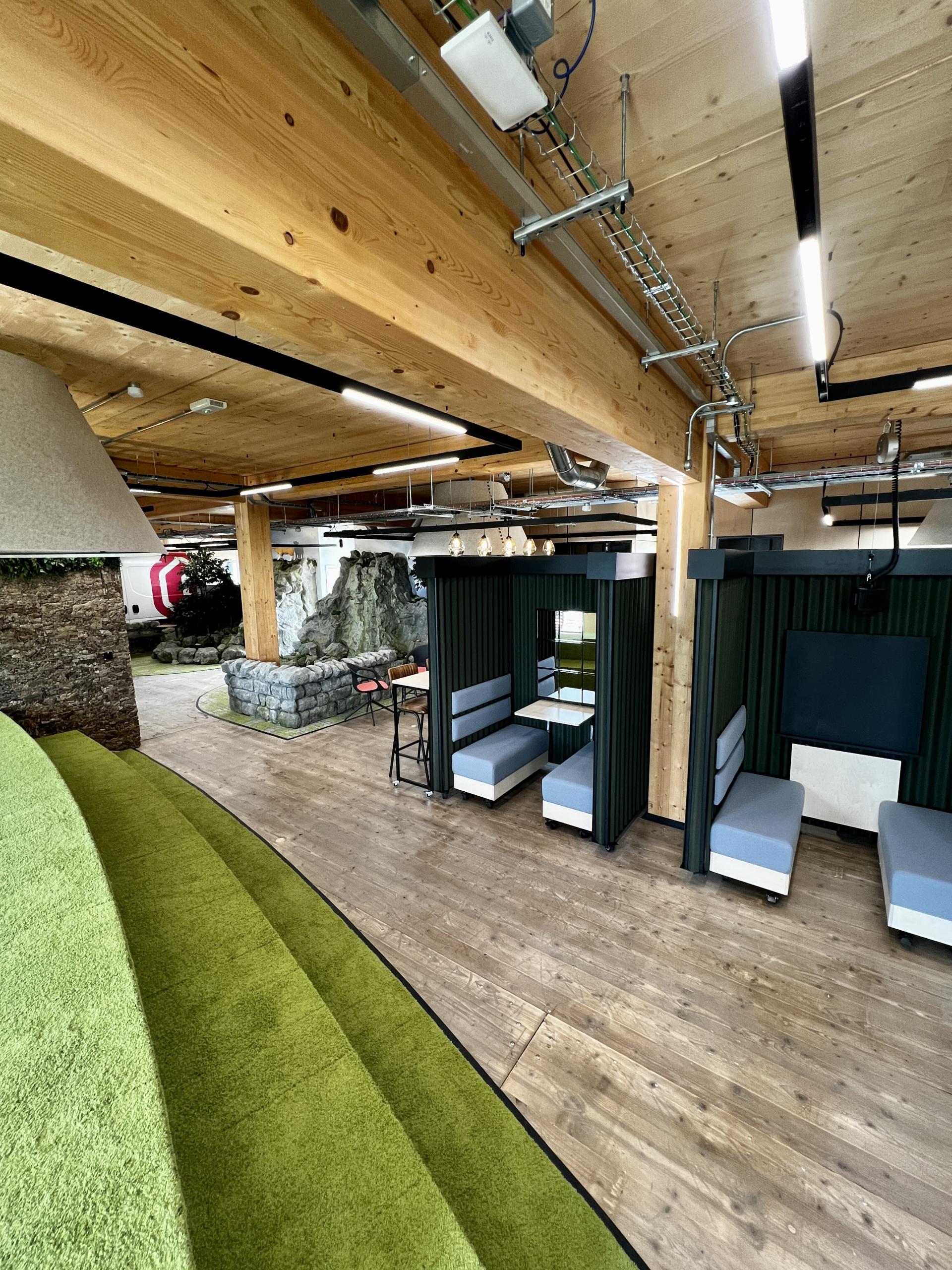 Modern net zero carbon workspace interior featuring green carpet seating, private meeting booths, and natural wood accents.