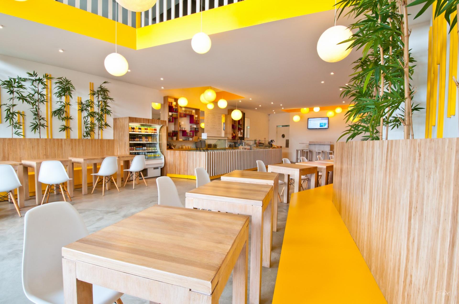 Brightly designed cafe interior featuring bamboo decor, wooden tables, and vibrant yellow accents, promoting sustainable practices.