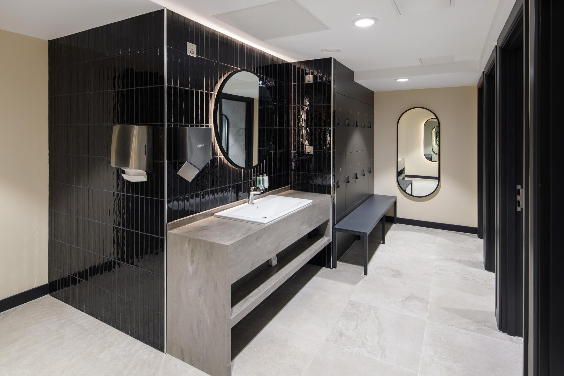 Renovated restroom at One Piccadilly Gardens featuring sleek black tiles, modern fixtures, and stylish mirrors by SpaceInvader.